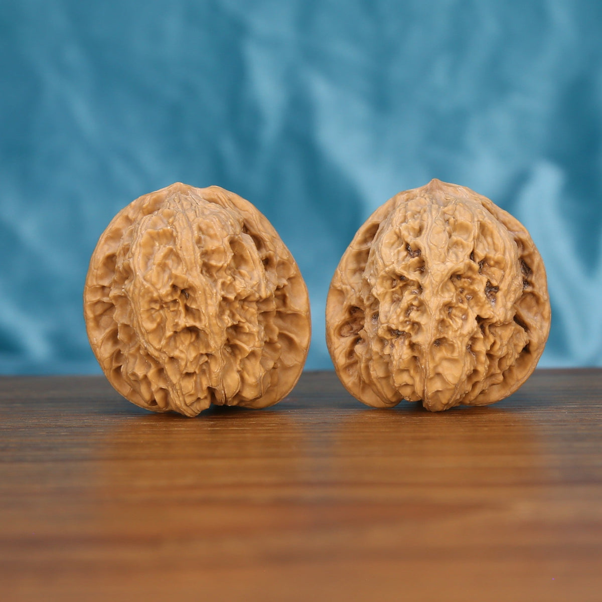 Pair of handcrafted wenwan walnuts side view on wood, blue background – matching grain pattern

