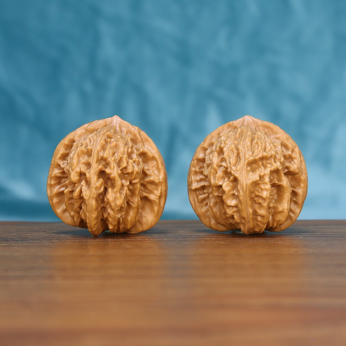 Pair of Coiling Dragon Wenwan walnuts standing upright on a wooden surface against a blue background
