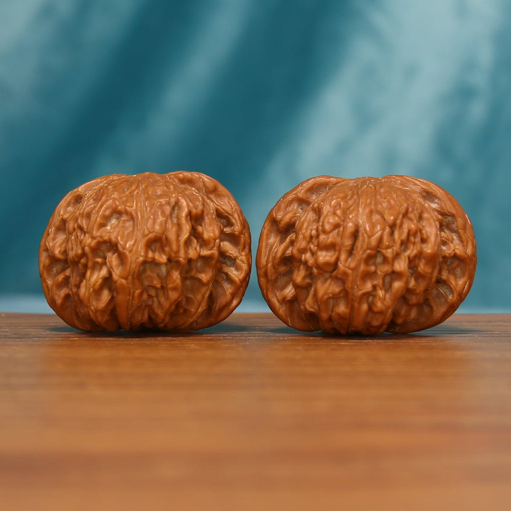 A pair of Millstone Wenwan walnuts shown from the front on a wooden tabletop
