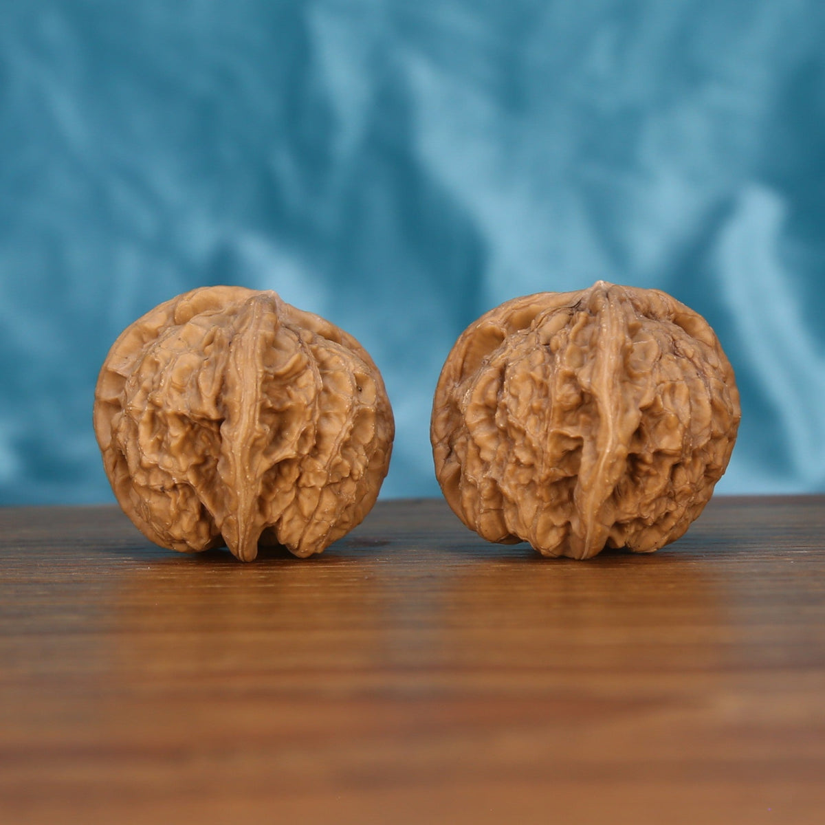 Two Duo-Leng Yuan-Bao wenwan walnuts on wooden surface, blue fabric background – matching sculpted ingots set