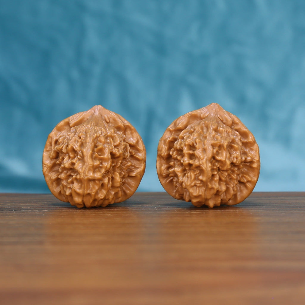 Pair of Qinhuangdao Ingot wenwan walnuts with rounded ingot shape and dense relief carving on a wood table against a blue background
