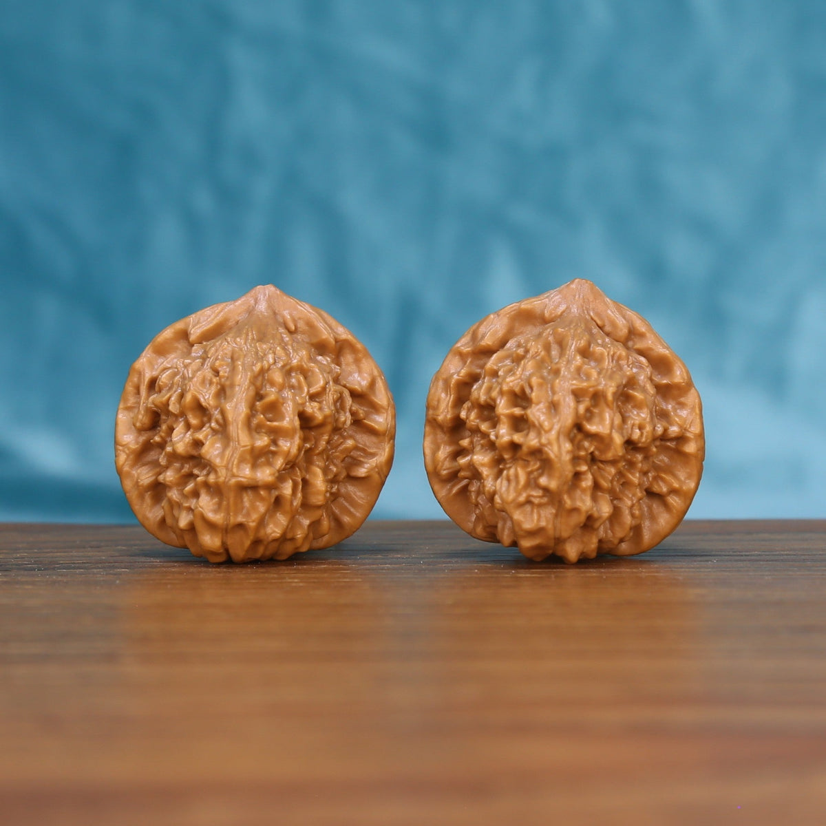 Pair of Qinhuangdao Ingot wenwan walnuts with rounded ingot shape and dense relief carving on a wood table against a blue background
