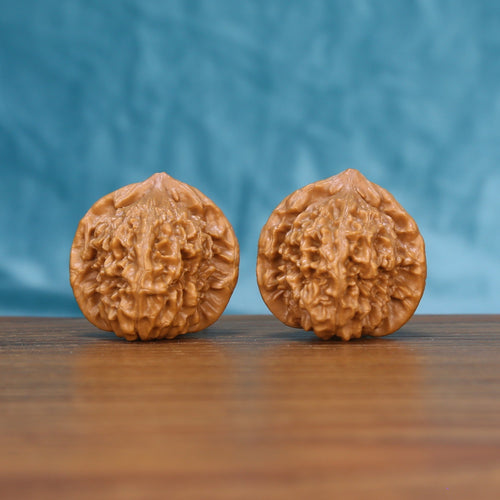 Pair of Qinhuangdao Ingot wenwan walnuts with rounded ingot shape and dense relief carving on a wood table against a blue background
