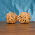 Two Da-Cu-Jin wenwan walnuts on wooden surface, blue fabric background – matching earthborn monoliths set