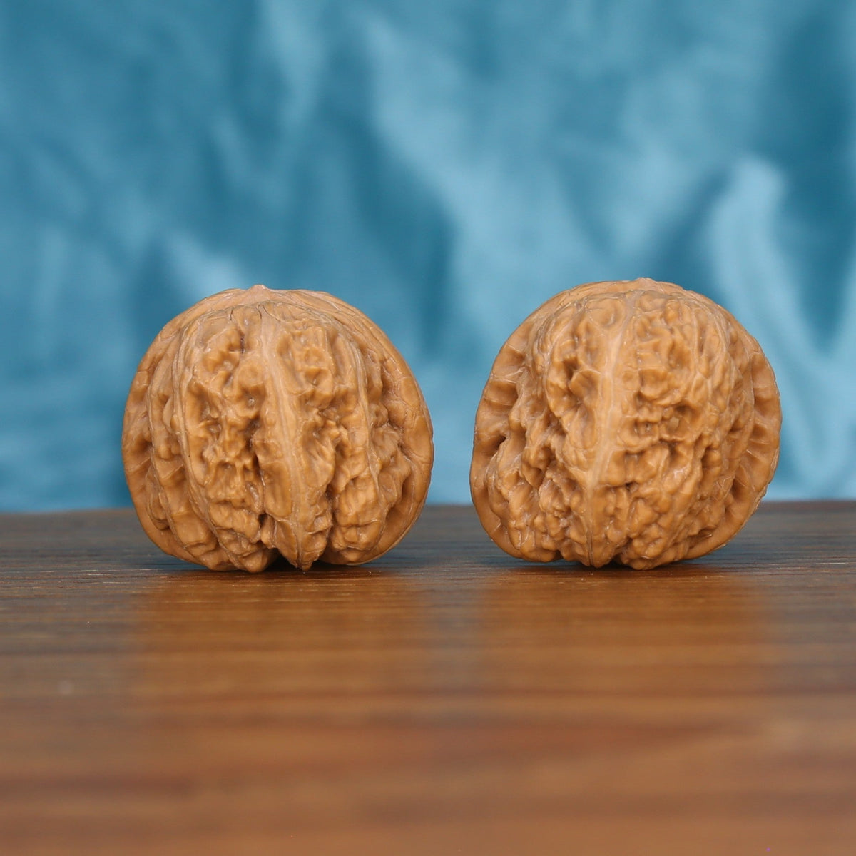 Two Ping-Gu-Yuan-Bao wenwan walnuts on wooden surface, blue fabric background – matching wealth-curve set