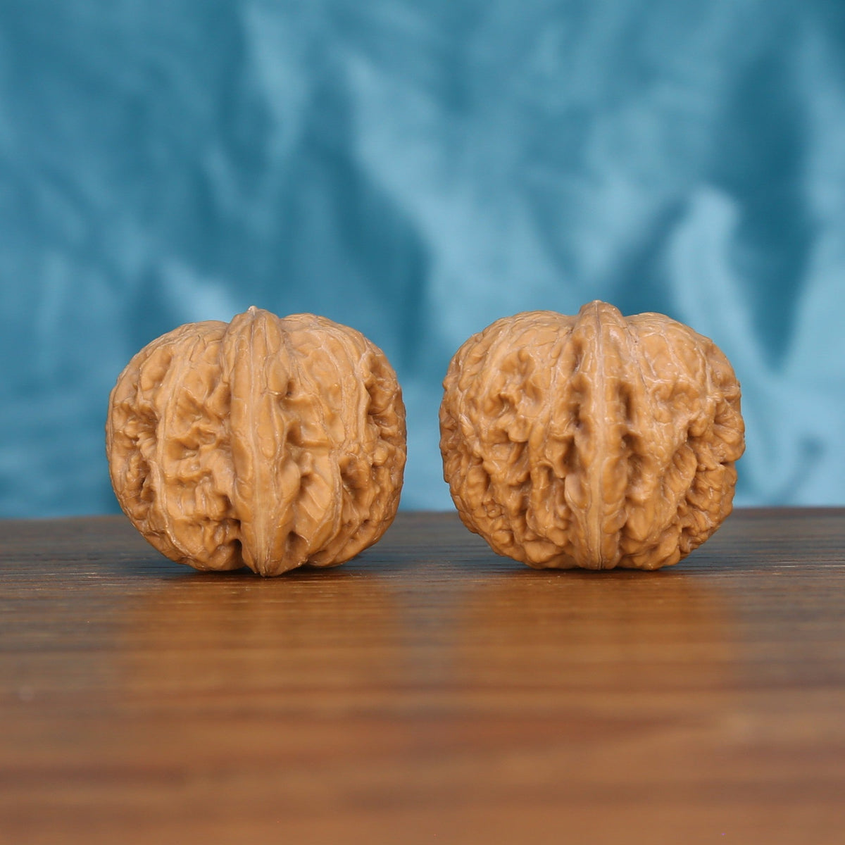 Ping-Gu-Yuan-Bao walnut set side profile on wood, blue background – symmetrical wealth-curve grain detail