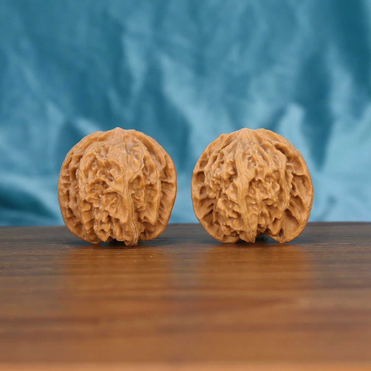 Ping-Guo-Yuan walnut set side profile on wood, blue background – symmetrical apple-round grain detail