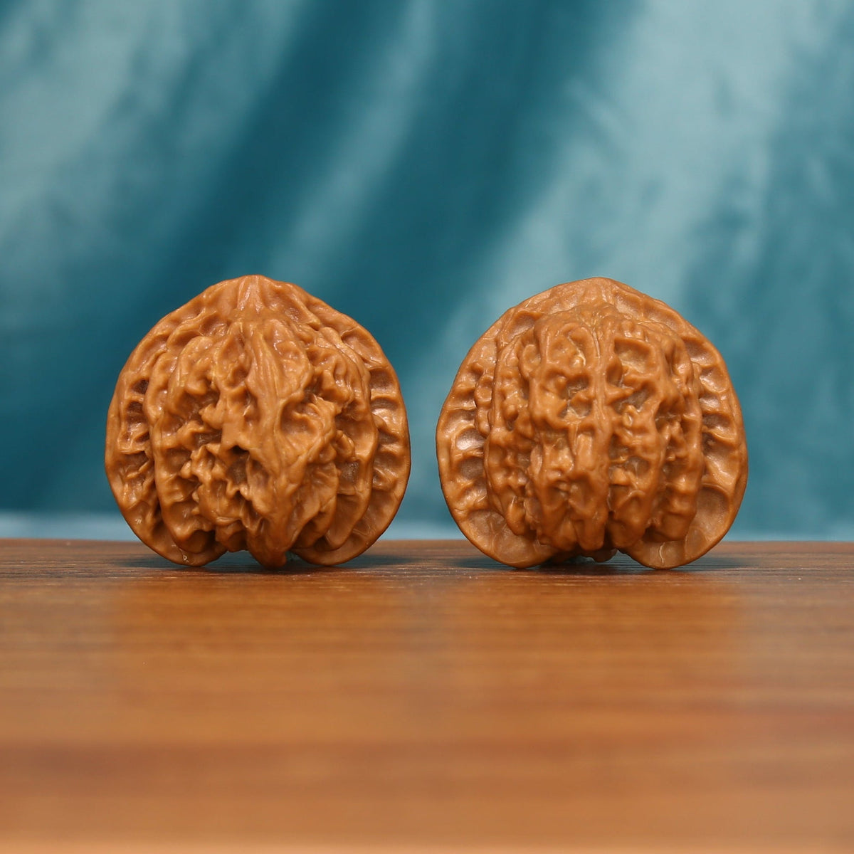 A pair of Apple Orchard Wenwan walnuts shown from the front on a wooden tabletop
