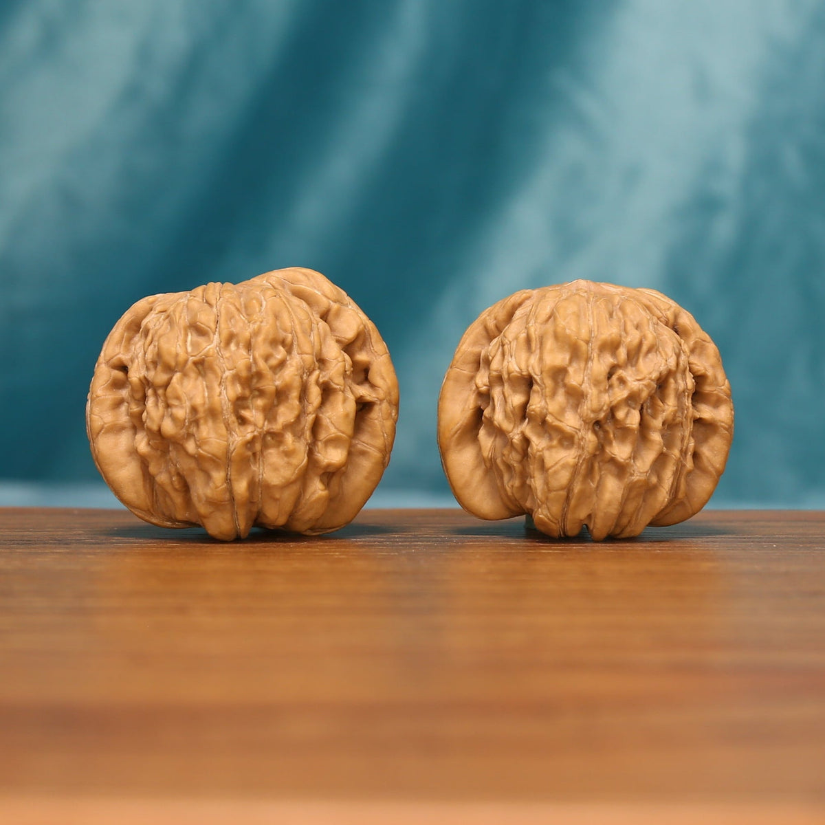 A pair of Huakun Dragon Wenwan walnuts shown from the front on a wooden tabletop
