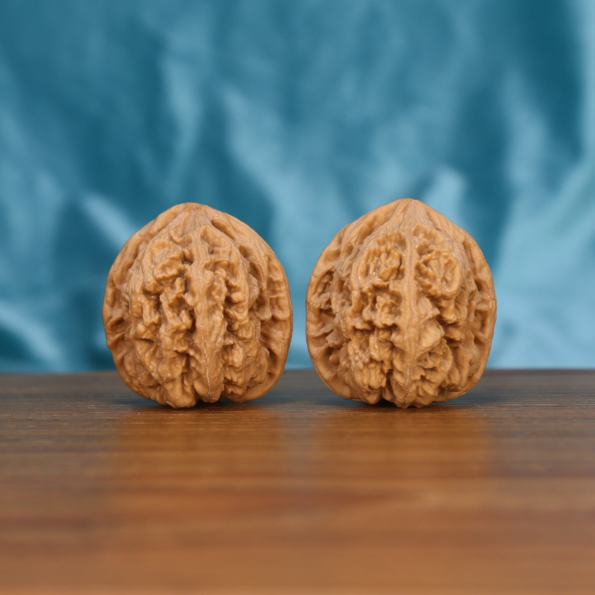 Two Da-Cu-Jin wenwan walnuts on wooden surface, blue fabric background – matching earthborn monoliths zen set