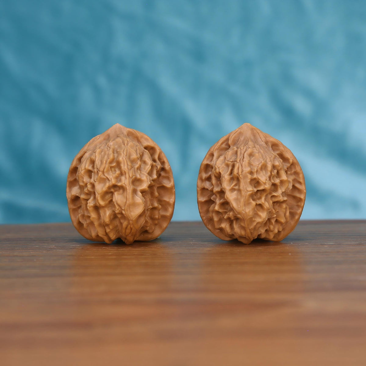 A perfectly matched pair of highly textured Wenwan Walnuts resting on a warm wooden surface against a tranquil blue backdrop. Serving as a tangible physical anchor and tactile meditation tool for digital detox.