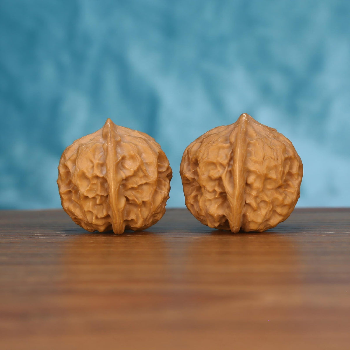 Pair of wenwan walnuts with smooth rounded form and central seam, side view on wooden surface